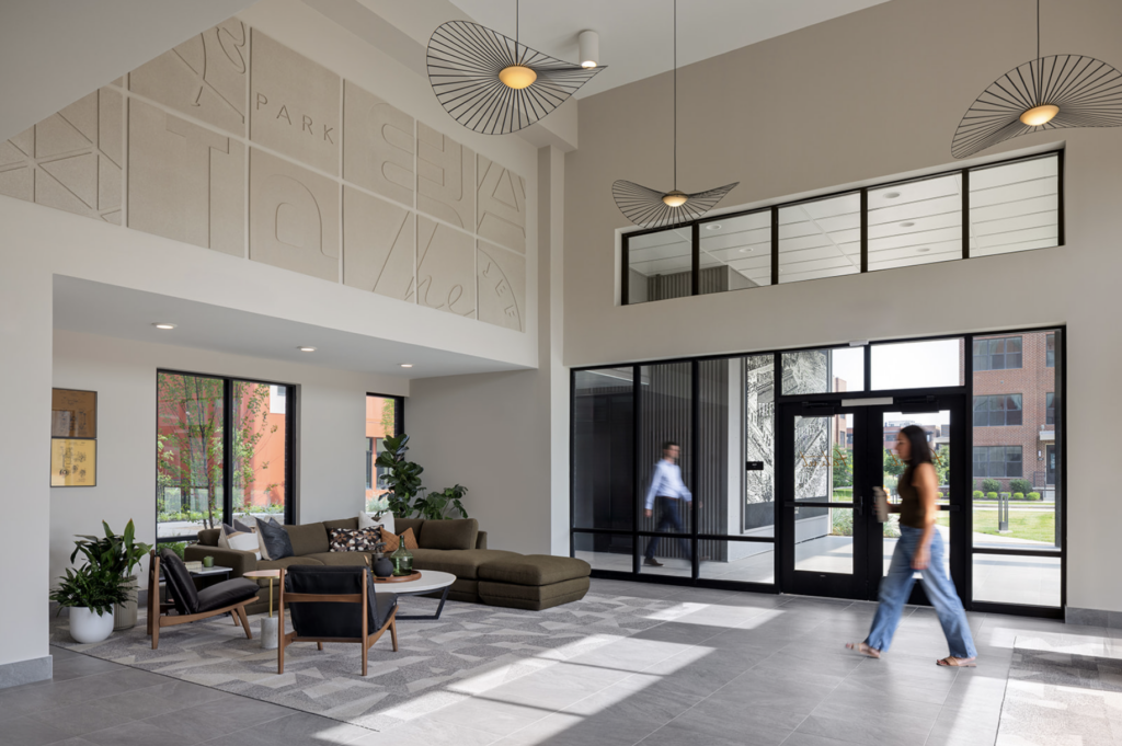 Thrive Companies, Modern office lobby with seating area, decorative wall art, large windows, pendant lights, and signage promoting the Resident Referral Program as two people walk near the entrance. Apartments in Columbus Ohio