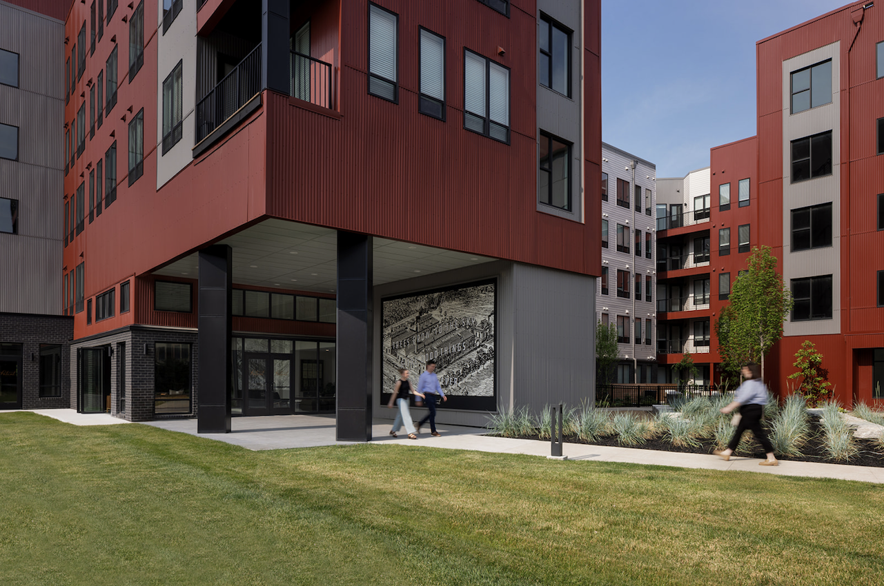 Thrive Companies, Modern apartment buildings by Thrive Companies Ohio feature red and gray exteriors, a landscaped grass area, and three people walking along a path near a large mural. Apartments in Columbus Ohio