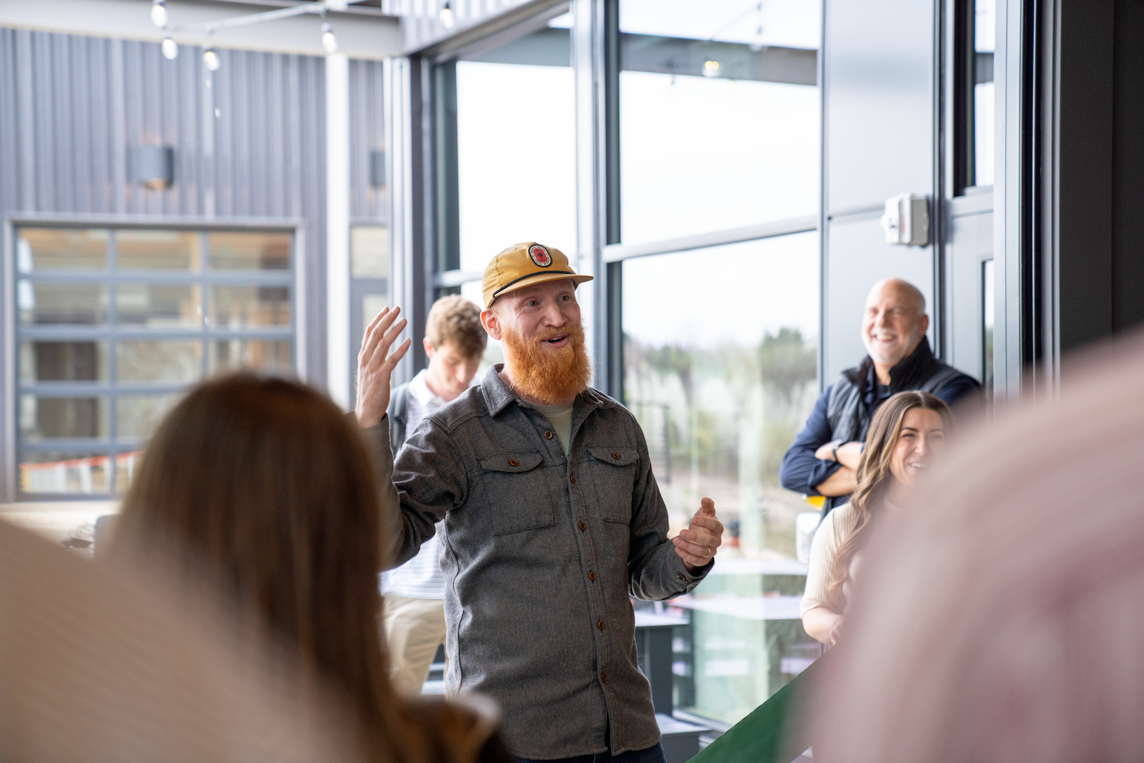 Thrive Companies, A man with a red beard and a cap gestures while speaking to a group indoors at a Thrive Companies event; people in the background watch and listen. Apartments in Columbus Ohio
