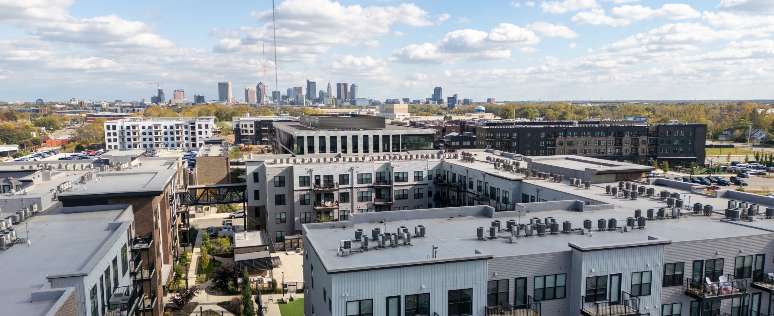 Thrive Companies, Aerial view of modern apartment buildings in the foreground, featuring our Preferred Employer Program, with a city skyline and scattered clouds in the background. Apartments in Columbus Ohio