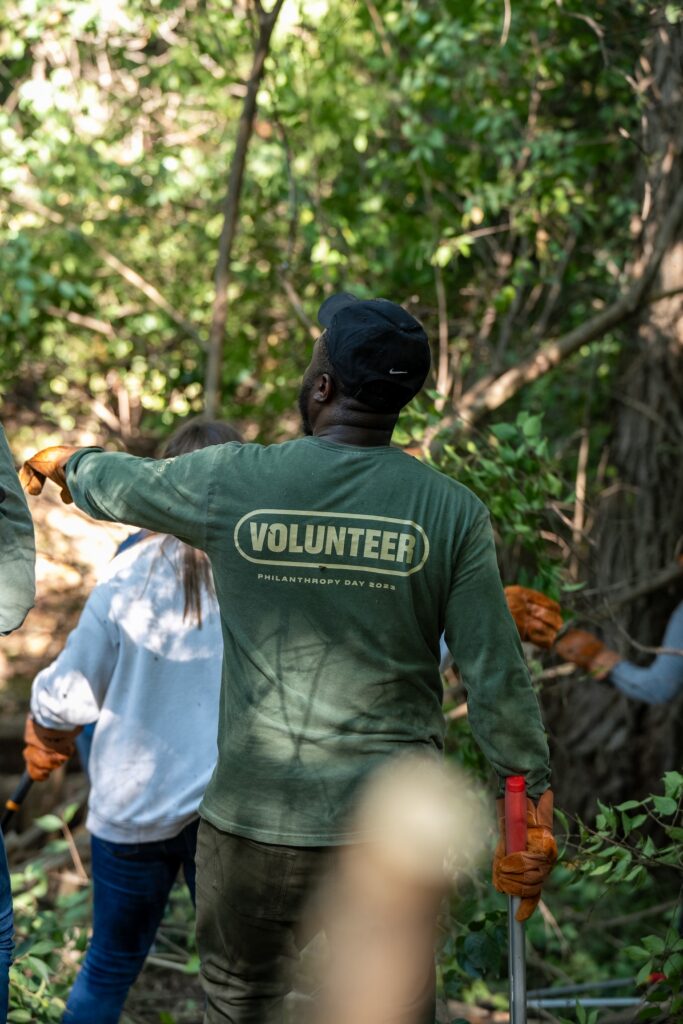 Thrive Companies, A group of people wearing gloves work outdoors in a wooded area; one person in a Volunteer shirt, part of Thrive Companies Ohio, gestures ahead. Apartments in Columbus Ohio
