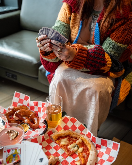 Thrive Companies, A person holding playing cards sits at a table with pizza, a pretzel, drinks, and more cards on red checkered paper—enjoying good times in true Thrive Companies style. Apartments in Columbus Ohio