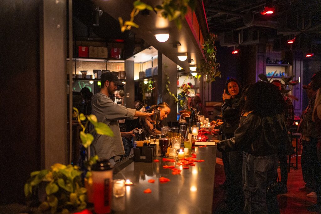 Thrive Companies, People are gathered at a dimly lit bar counter adorned with candles and red petals, fostering a sense of community management as they engage in lively conversation and drinks. Apartments in Columbus Ohio