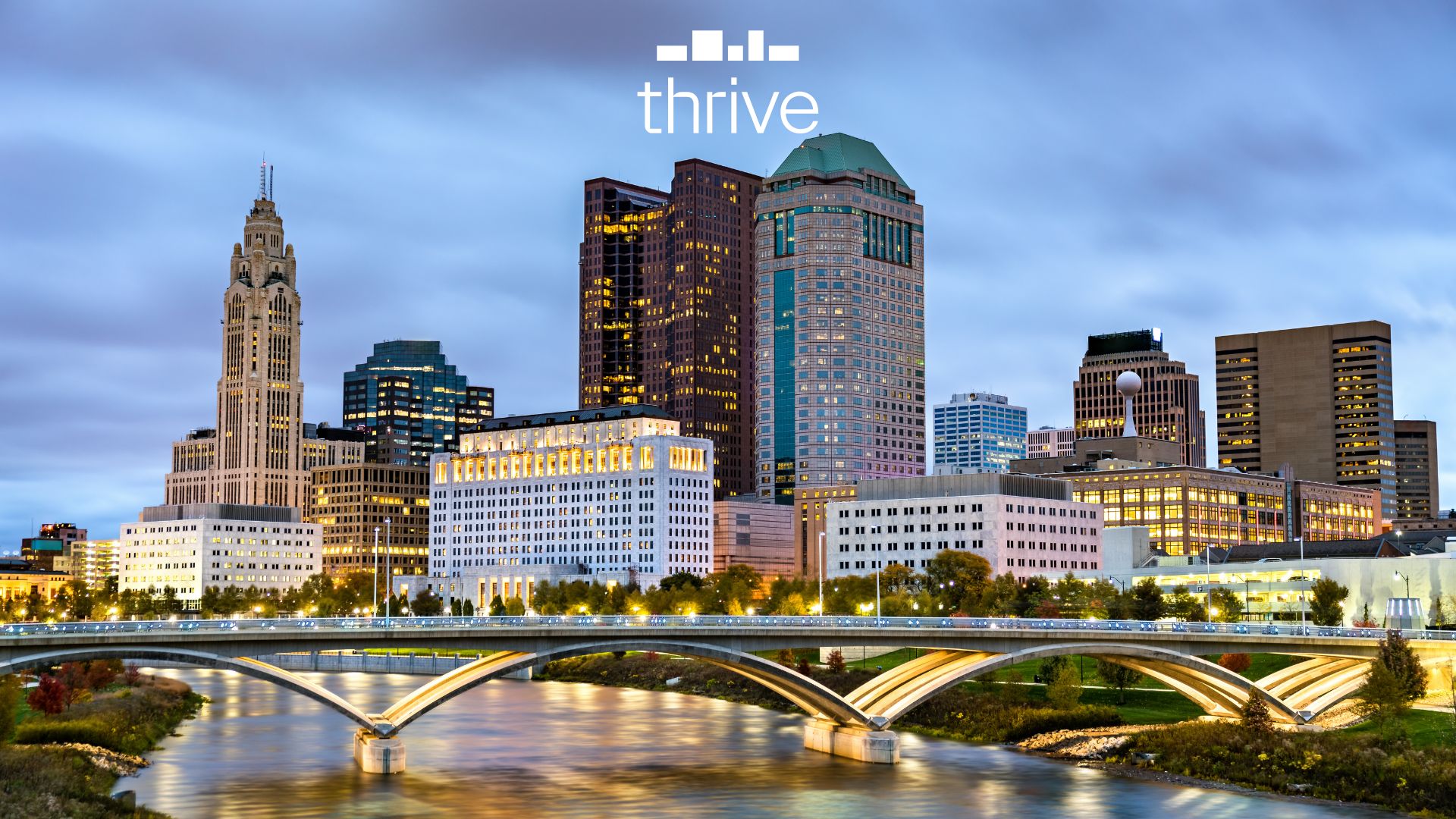 Thrive Companies, A city skyline at dusk with modern and historic buildings, a river and bridge in the foreground, set in the vibrant Franklinton Arts District, with the word thrive at the top. Apartments in Columbus Ohio