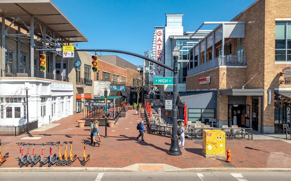 Thrive Companies, Outdoor urban shopping area with pedestrians, restaurants, scooters lined up, and prominent signage reading GATEWAY and HIGH ST under a clear blue sky. Apartments in Columbus Ohio