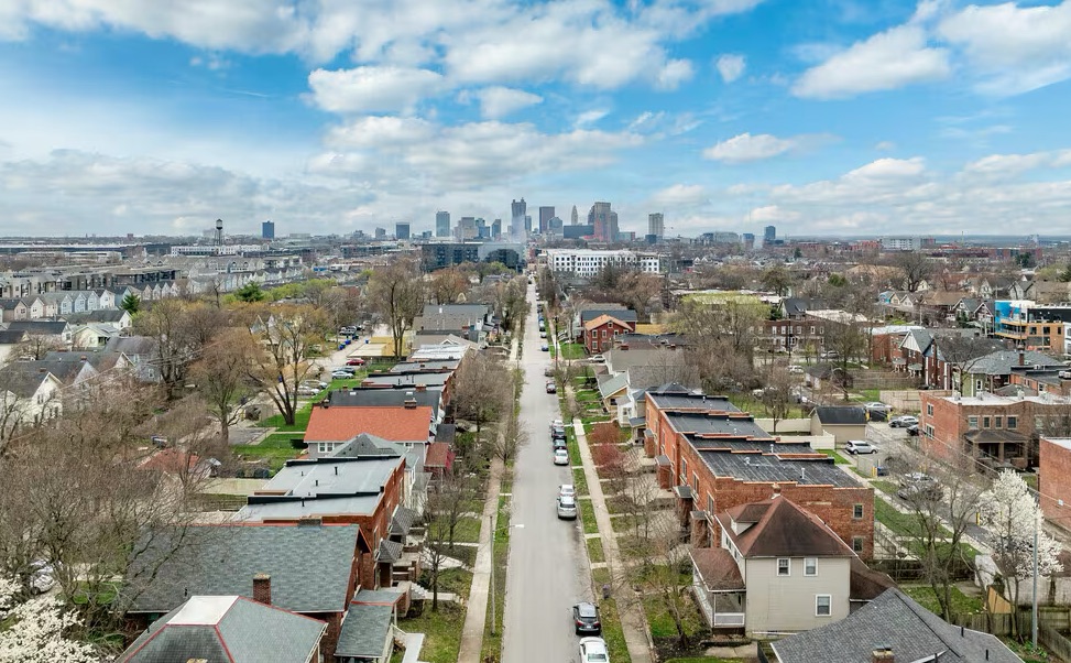 Thrive Companies, Aerial view of a residential neighborhood with tree-lined streets and houses, with a city skyline visible in the distance under a partly cloudy sky. Apartments in Columbus Ohio
