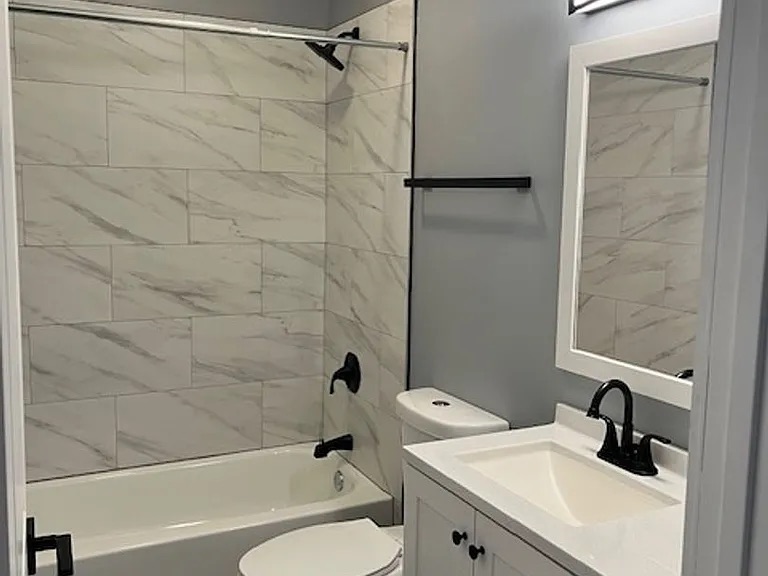 Thrive Companies, Modern bathroom with white marble tile above a bathtub, black fixtures, a white vanity, and a rectangular mirror with a white frame. Apartments in Columbus Ohio