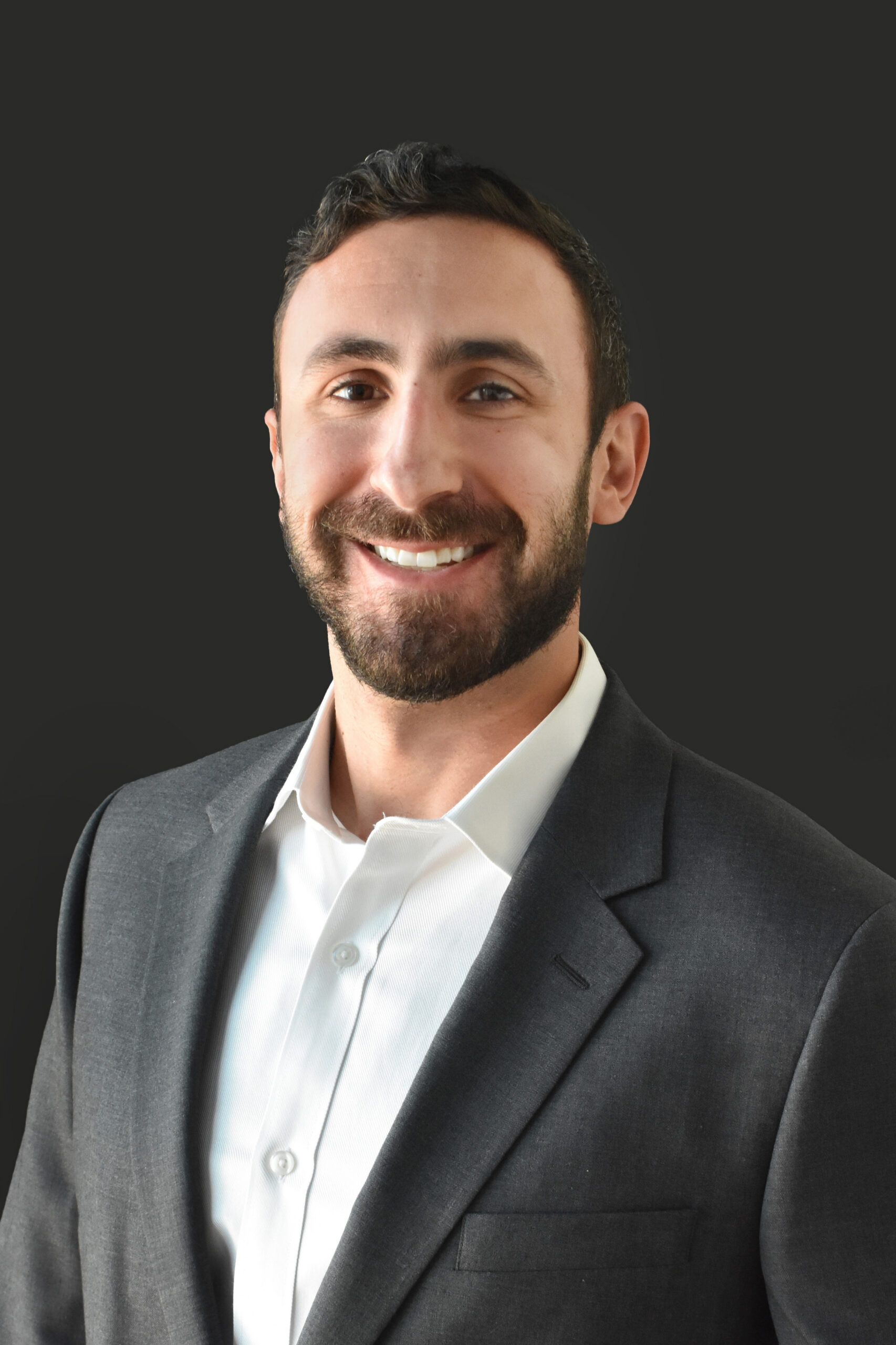 Thrive Companies, A member of Our Team, a man with short dark hair and a beard, wearing a white shirt and dark suit jacket, smiles at the camera against a plain dark background. Apartments in Columbus Ohio