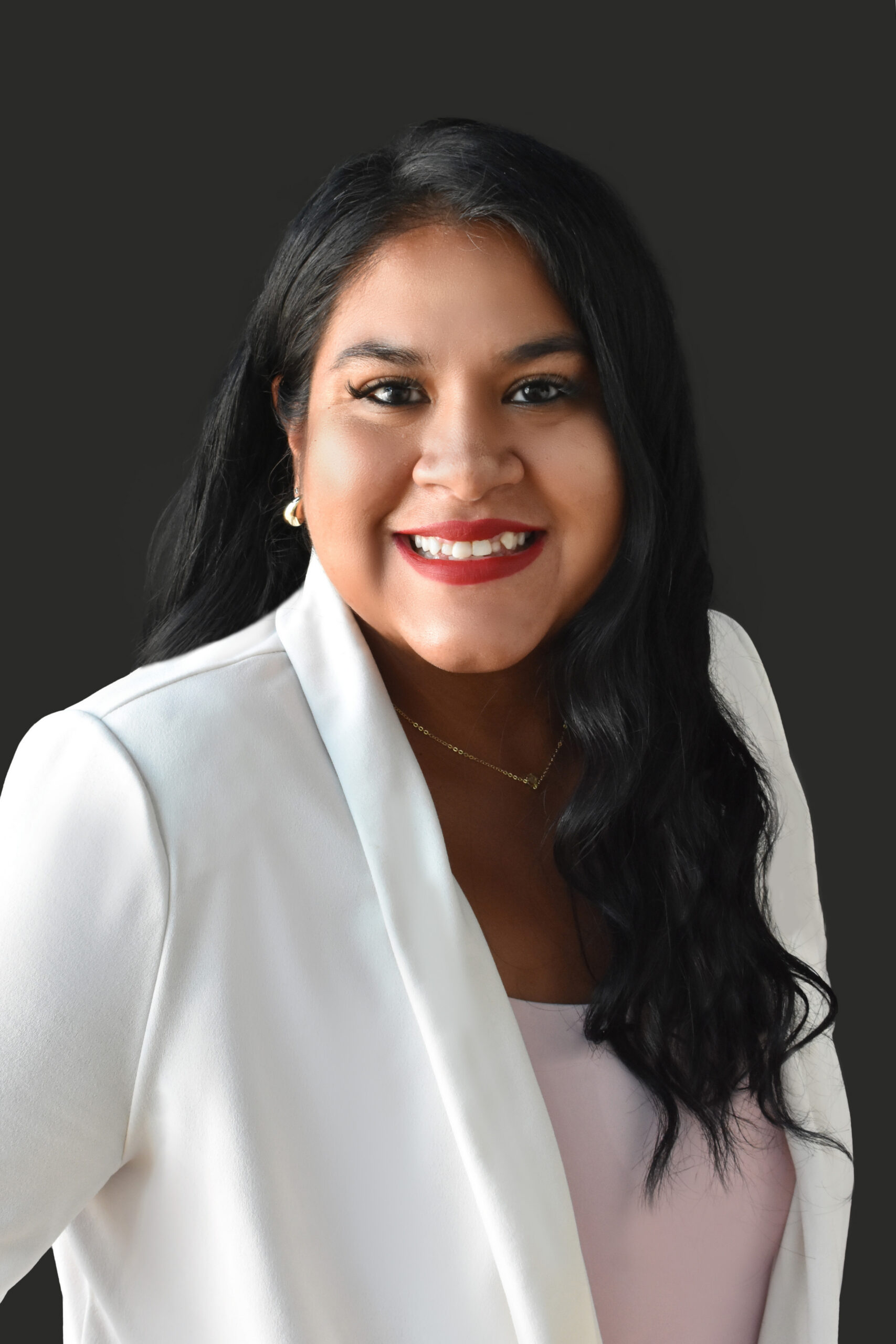 Thrive Companies, Our Team: Woman with long black hair wearing a white blazer and light pink top, smiling at the camera against a dark background. Apartments in Columbus Ohio