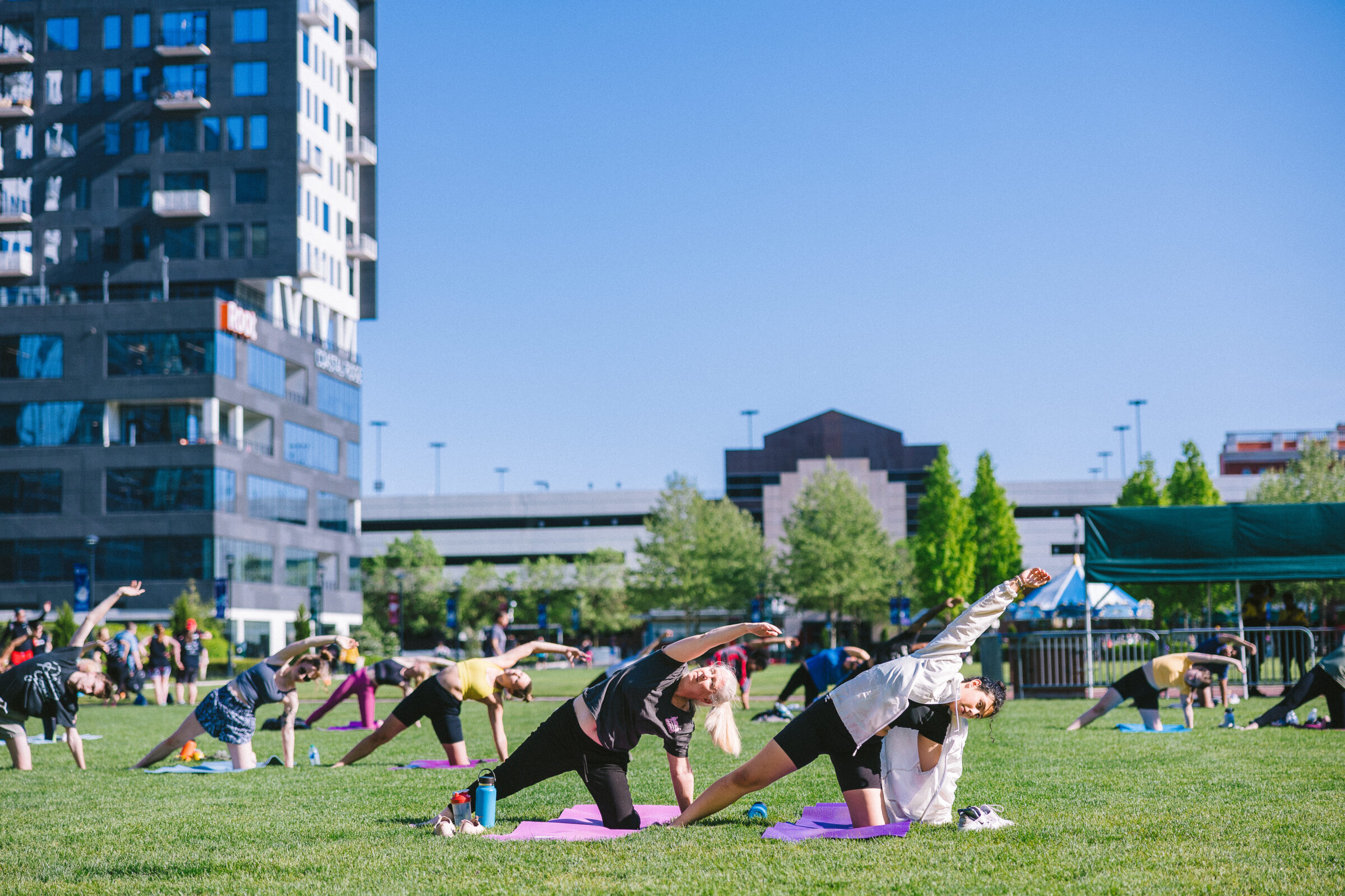 Thrive Companies, People practice yoga on mats in an outdoor park, surrounded by buildings, under a clear blue sky as part of the JP Resident Wellness Event. Apartments in Columbus Ohio