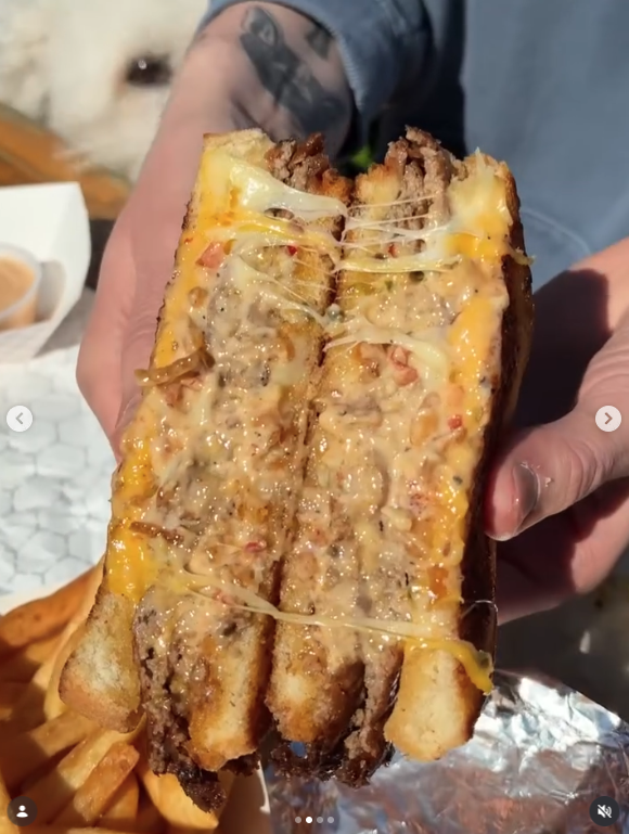 Thrive Companies, A person holds a gooey, cheesy sandwich cut in half, revealing a melty filling of cheese and meat—just the kind of indulgent comfort food you’d expect from Smash City Burgers—with crispy fries visible in the background. Apartments in Columbus Ohio