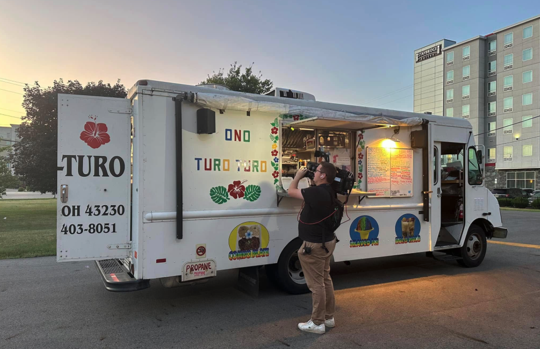 Thrive Companies, A person stands in front of the Ono Turo-Turo food truck with a camera, capturing the menu posted on the side. The truck is parked near a hotel at sunset. Apartments in Columbus Ohio