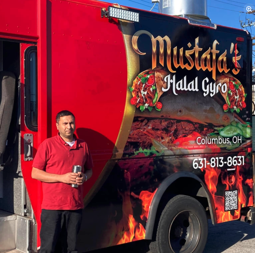 Thrive Companies, A man stands in front of a red food truck with the sign Mustafa’s Halal Gyro, Columbus, OH and a phone number displayed on the side, ready to serve delicious Halal Food. Apartments in Columbus Ohio