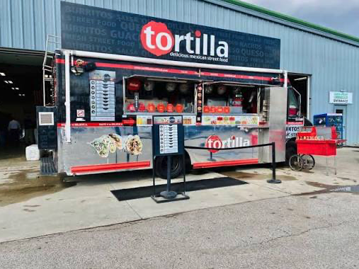 Thrive Companies, A Tortilla Street Food truck serves delicious Mexican street food outside a large building, with menu boards and a red popcorn cart nearby—a highlight of Food Truck Fridays. Apartments in Columbus Ohio