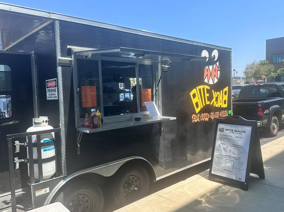 Thrive Companies, Black food truck labeled Bite Back with a menu board, condiments, and an open service window, parked on a sunny street—perfect for Food Truck Fridays. Apartments in Columbus Ohio