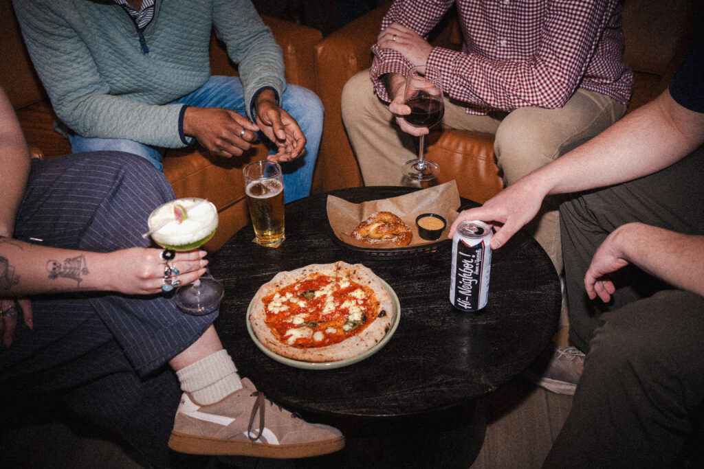 Thrive Companies, Four people sitting around a small table at Bada Bar with a margherita pizza, a pretzel, and various drinks during a tasting. Apartments in Columbus Ohio